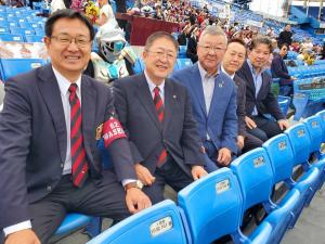 市長ら関係者5名がスタンド席に座りカメラに笑顔を向けている写真