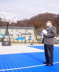 新しくうみどり公園に設置されたバスケットボールコートの前で、マイクを持った市長が挨拶を行っている完成記念イベントの様子の写真