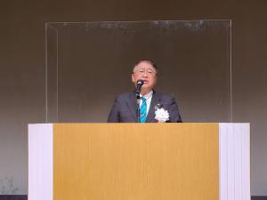 パーテーションが設置された壇上で挨拶を行っている市長の写真