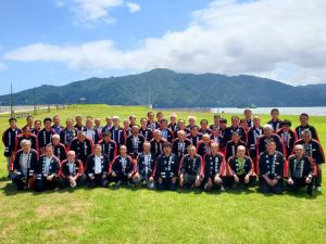 後ろに大きな山が見える広大な芝生の公園で法被を着た消防団の方々40名程が並んでいる集合写真