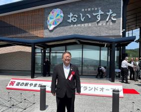 おいすたの入り口前に立つスーツを着て胸章をつけた市長の写真