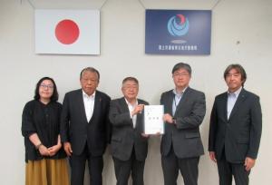2枚の旗が掲げられた壁の前で、中央に岩手河川国道事務所の近藤修所長と市長が一緒に要望書を持ち、3名の関係者が横一列に並んでいる写真