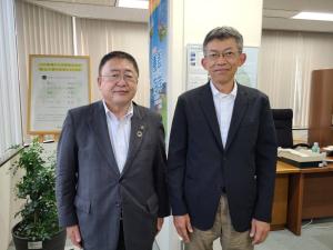 大きなポスターや地図が掲示された室内で、環境省東北地方環境事務所の田村省ニ所長と市長が並んでいる写真
