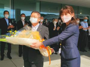 整列し拍手をしている職員たちの前で、女性職員から花束を受け取る市長の写真