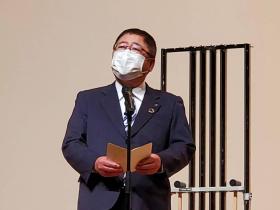 市長がステージ上で、鐘の楽器の前で式辞を述べている写真