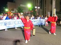 赤色の衣装を着た市長と関係者が、提灯を片手に道路を歩いている写真