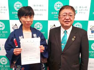 任命書を両手で持ち正面に掲げる女性とその横で笑顔を浮かべる市長の写真