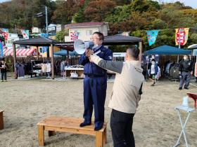 市長が公園内の芝生に置かれた台の上に立ち、拡声器を使ってあいさつをしている写真