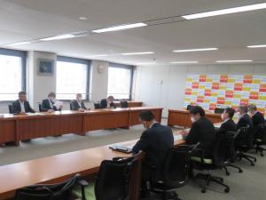 大きな窓ガラスが設置された会議室で、向かい合って着席した関係者が意見交換を行っている様子の写真