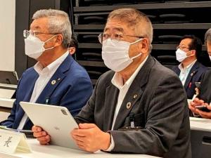 マスクをつけた関係者が自席に座り、タブレットを両手で持った市長が話を聞いている様子の写真
