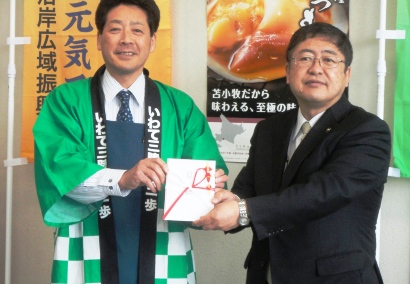 緑色の半被を着た「とまこまい味な倶楽部」の代表の男性と市長が一緒に金封を持って記念撮影している写真