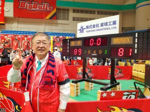 得点が表示されたモニターの前で右手の人差し指を上に向けポーズを決める市長の写真