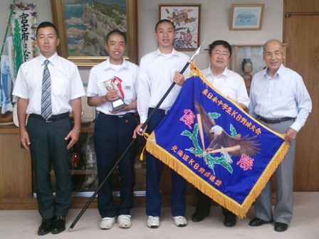 市長と東日本中学生KB野球大会の優勝旗とトロフィーを手に持った中学生と関係者が5名並んでいる写真