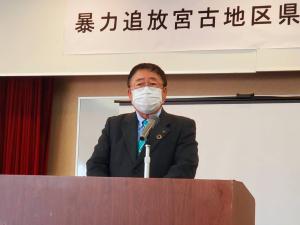 「暴力追放宮古地区県民会議研修会」と書かれた横断幕やスクリーンが設置された会場で、檀上に立つ市長が挨拶を行っている写真