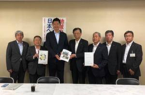 市長や自民党の関係者らスーツ姿の男性7名が横一列に並び左から2番目~5番目の男性が要望書などの書類を持っている写真