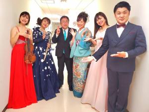 市民文化会館の廊下で「ふるさとに贈る2022」の出演者(金澤未咲さん、福寄屋濤太衛門(中川太治)さん、グラツィアの皆さん)に囲まれて並んでいる市長の写真