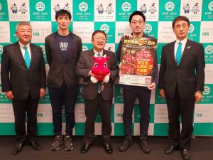 バックパネルの前で「岩手ビッグブルズ」のマスコットキャラクターブルゾーのぬいぐるみを持った市長を中央に、水野社長と関係者の男性、2名の市の関係者の男性が横一列に並んでいる写真