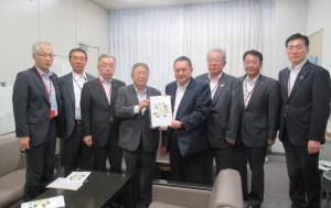 市長や国土交通省の関係者らスーツ姿の男性8名が横一列に並び中央に立つ2名が2人で要望書を持っている写真