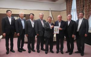 市長や財務省の関係者らスーツ姿の男性8名が横一列に並び中央に立つ2名が2人で要望書を持っている写真