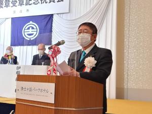 祝賀会会場のステージ下に設置された檀上のマイクの前で、市長が挨拶を行っている様子の写真