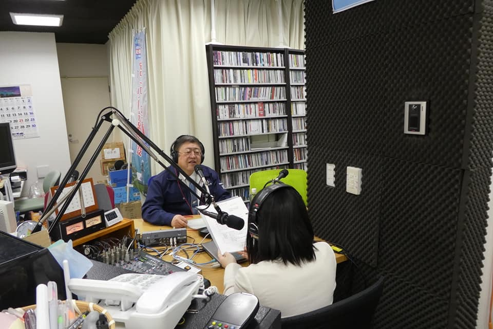 スタジオの中でヘッドホンを着けてマイクの前でパーソナリティの女性と向かい合って話す様子の市長の写真