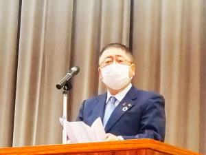 マスクをつけた市長がマイクが設置された壇上で挨拶を行っている入学式の様子の写真