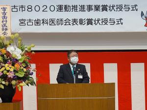 「宮古市8020運動推進事業賞状授与式」と書かれた横断幕と紅白幕が掲げられた檀上で、市長が挨拶を行っている様子の写真