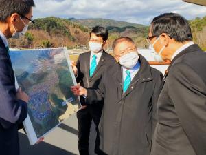 市長が小島敏文副大臣に職員2人が広げた写真をみせながら、説明している写真