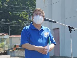 青いポロシャツを着た市長がスタンドマイクの前で話をしている様子の写真