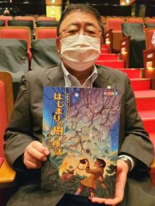 椅子に座りミュージカルのパンフレットを両手で持ち正面に向けている市長の写真