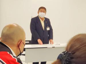 目の前に置かれたテーブルに両手を軽くついて立ちながら話をする様子の市長の写真