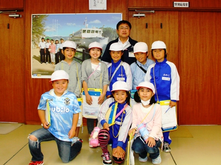 市長の前に生徒5名が立ち、その前には3名の生徒が膝立ちして室内で記念撮影している写真