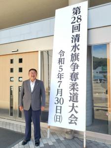 「第2改清水旗争奪柔道大会 令和5年7月30日(日曜日)」と書かれた大きな立て看板の横に立つ市長の写真