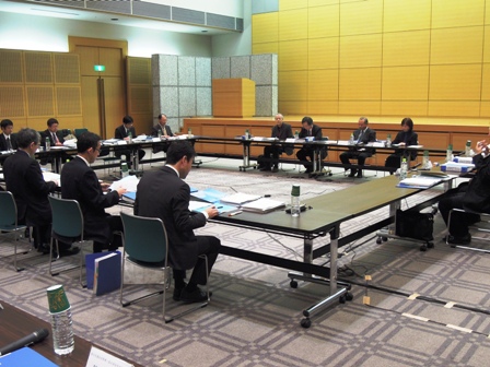 ステージがある絨毯が敷かれた会場で口の字に机を並べ関係者たちが座り話し合いをしている写真