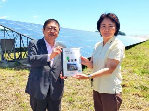 大きな太陽光パネルの前で、山田美樹環境副大臣と市長が要望書を一緒に持っている写真