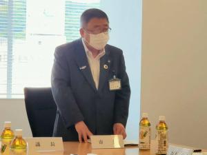 「市長」と書かれたプレートが置かれた机の前に立ち、話をしている様子の市長の写真