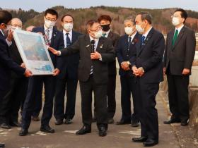 関係者の方々が見ている中、市長が菅義偉内閣総理大臣に、職員が持っている地図を指さしながら、復興状況を説明している写真