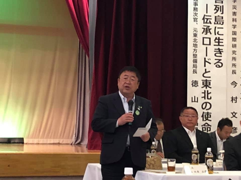 ステージ前に設置された自席から立ち上がり、右手にマイクを持った市長が話をしている総会の様子の写真