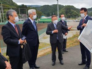 道路脇で、写真パネルのようなものを持っている男性と、そのパネルを見ながら説明をする様子の市長、話を聞く3名の男性を写した写真