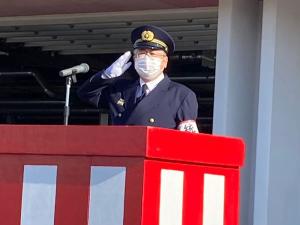 紅白に塗装された演台の前で制服と制帽を身に着け、白い手袋を着けた右手で敬礼をしている様子の市長の写真