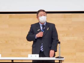 市長が会長と書かれた卓上プレートの席で立ち、今年度の事業実績や来年度事業について述べている写真