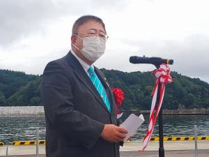 港で紅白リボンが着けられたスタンドマイクの前で手紙を読む様子の市長の写真