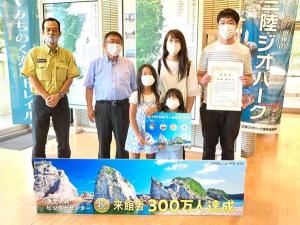 「来館者300万人達成」という文字と浄土ヶ浜の写真が載っているパネルの後方で、賞状を持つ父親と母親、女の子2人の家族が立ち、その隣で市長と関係者の男性1名が立っている記念写真
