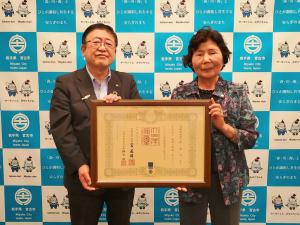 市長が春の叙勲「藍綬褒章」の受章された鈴木光子さんと受賞の賞状を持っている写真