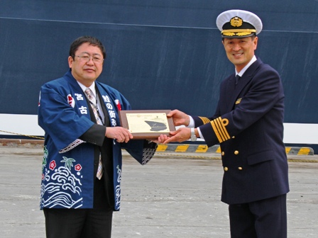 久葉誠司船長が大漁旗の記念品をはっぴ姿の市長へ手渡している写真