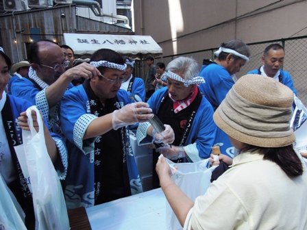 半被をきた市長が両手でサンマをつかみ女性が広げている袋にいれようとしている写真