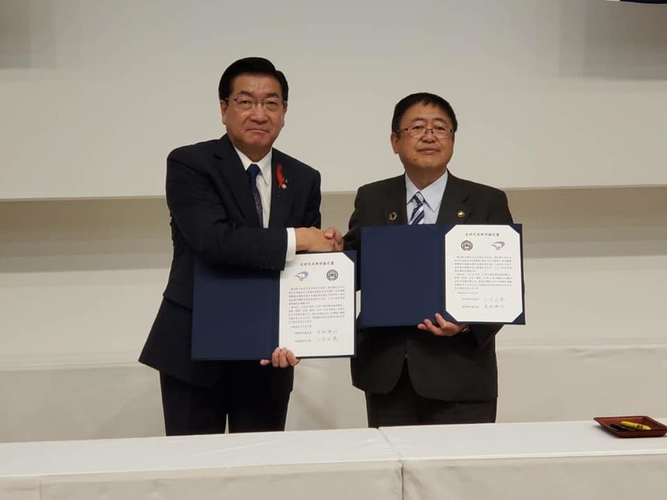 片手で締結書を持ち、反対の手で握手をする様子の市長と関係者の男性の記念写真