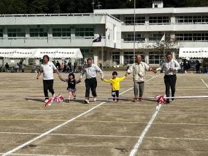 左から、男性、小さな女の子、市長、小さな男の子、男性、男性の6人が手をつないでグラウンドを走り、ゴールテープを切ろうとしている場面の写真