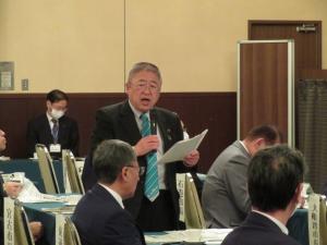 右手にマイク、左手に資料を持ち椅子に座って参加している方達に向けて話す市長の写真