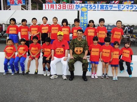 1列目に山本市長、滝澤幕僚長を中心に赤いTシャツ姿の子供が4人ずつ両脇に並び、その後ろに10人の赤いTシャツを着た子供達が並んだ集合写真